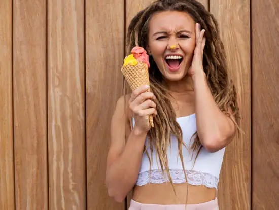 young sexy blonde girl with dreads eating multicolored ice cream in waffle cones in summer evening cries holding her head - dreadlocks extensions
